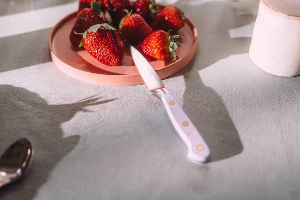 Plate of strawberries and a knife on a light-colored tablecloth, with sunlight casting soft shadows.