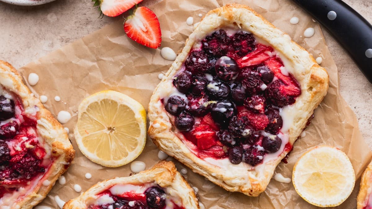 Mixed berry danishes laying on counter with a WÜSTHOF Classic Ikon knife and sliced fruit